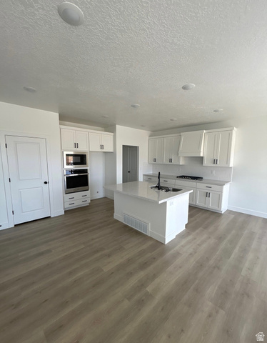 Kitchen with white cabinetry, stainless steel appliances, a center island with sink, light wood-style flooring, and a textured ceiling
