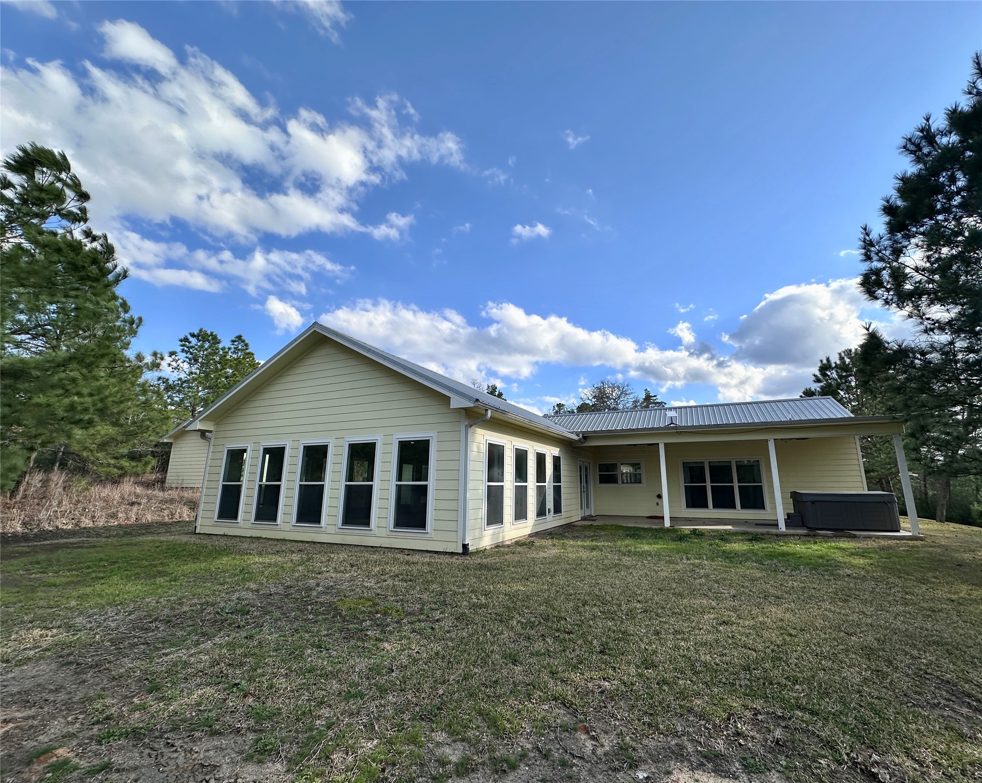 124 Pine Path Bastrop, TX 78602 - Photo 27 of 31 Rear view of house featuring metal roof, a lawn, a patio, and a hot tub