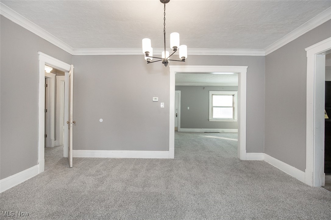 1045 Carlyon Road Cleveland, OH 44112 - Photo 6 of 26 Unfurnished dining area featuring ornamental molding, carpet, a chandelier, and a textured ceiling