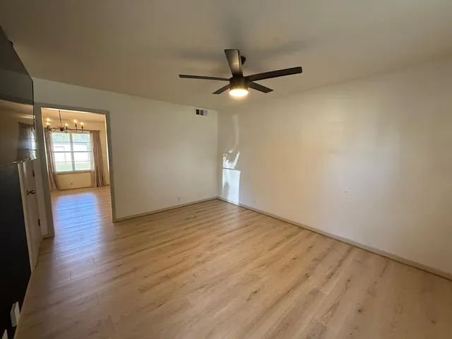 an empty room with wooden floor fan and windows