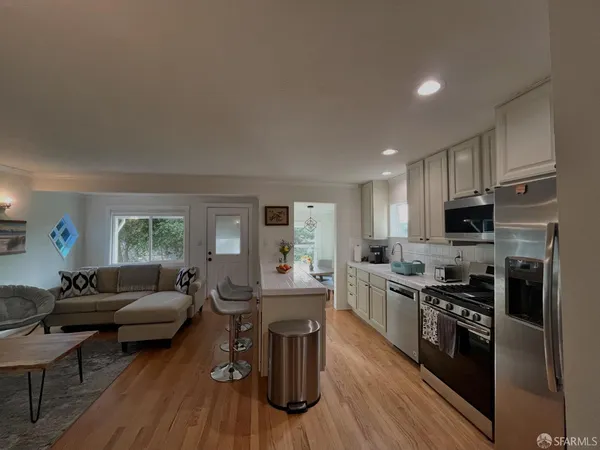 a living room with stainless steel appliances furniture and a wooden floor