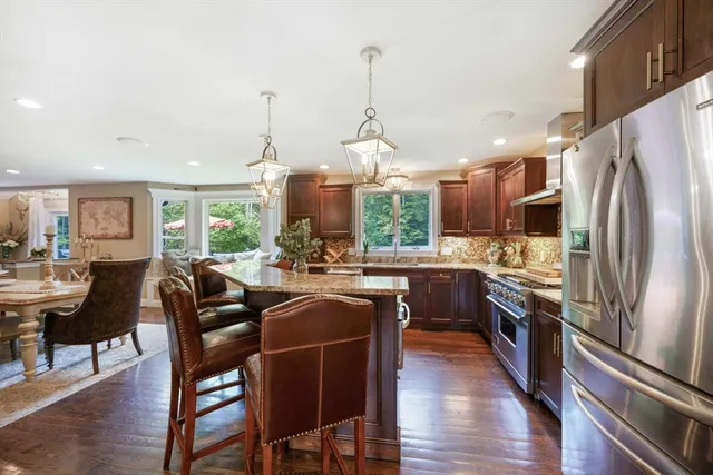 a kitchen with stainless steel appliances granite countertop a refrigerator a stove a sink a dining table and chairs with wooden floor