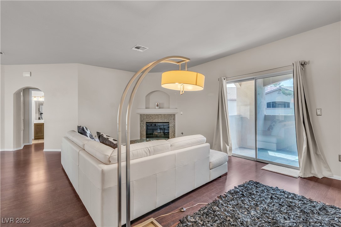 2050 West Warm Springs Road, Unit 1822 Henderson, NV 89014 - Photo 12 of 55 Living area with a glass covered fireplace, baseboards, visible vents, dark wood finished floors, and arched walkways and access to slate tiled balcony that connects to Primary Bedroom.