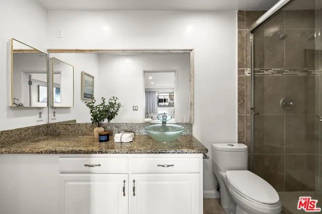 a bathroom with a granite countertop sink a toilet a mirror and shower