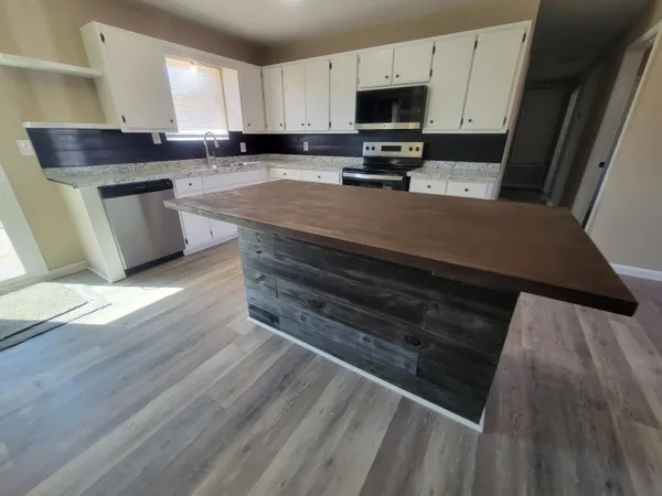 a kitchen with stainless steel appliances a stove a sink a microwave a refrigerator a stove and white cabinets