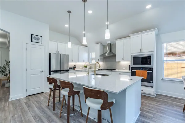 a kitchen with stainless steel appliances granite countertop a stove a refrigerator a oven a sink a dining table and chairs with wooden floor