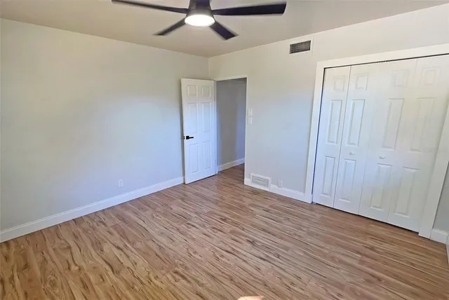 an empty room with wooden floor closet and windows