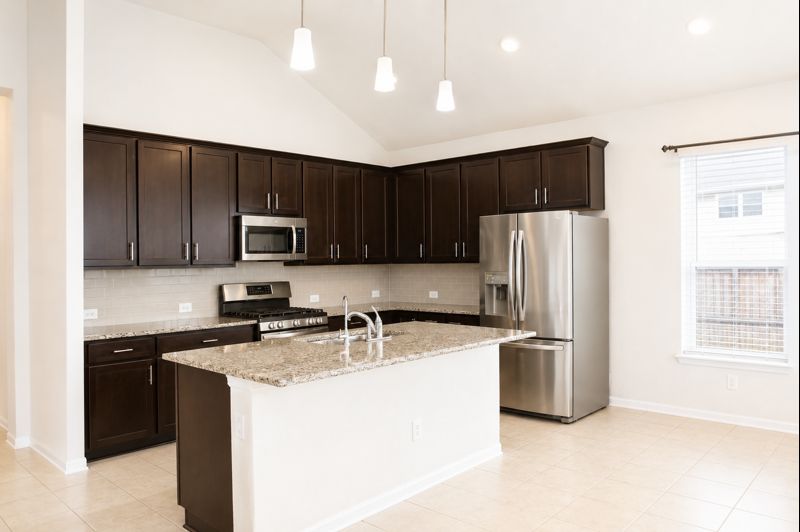 693 Durian Loop Buda, TX 78610 - Photo 8 of 27 Culinary adventures await in this kitchen featuring an inviting island and elegant dark wood cabinetry.