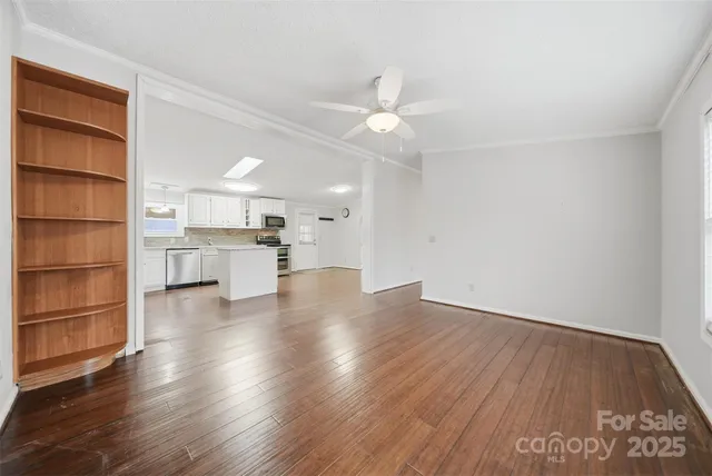 an empty room with wooden floor kitchen view and a window