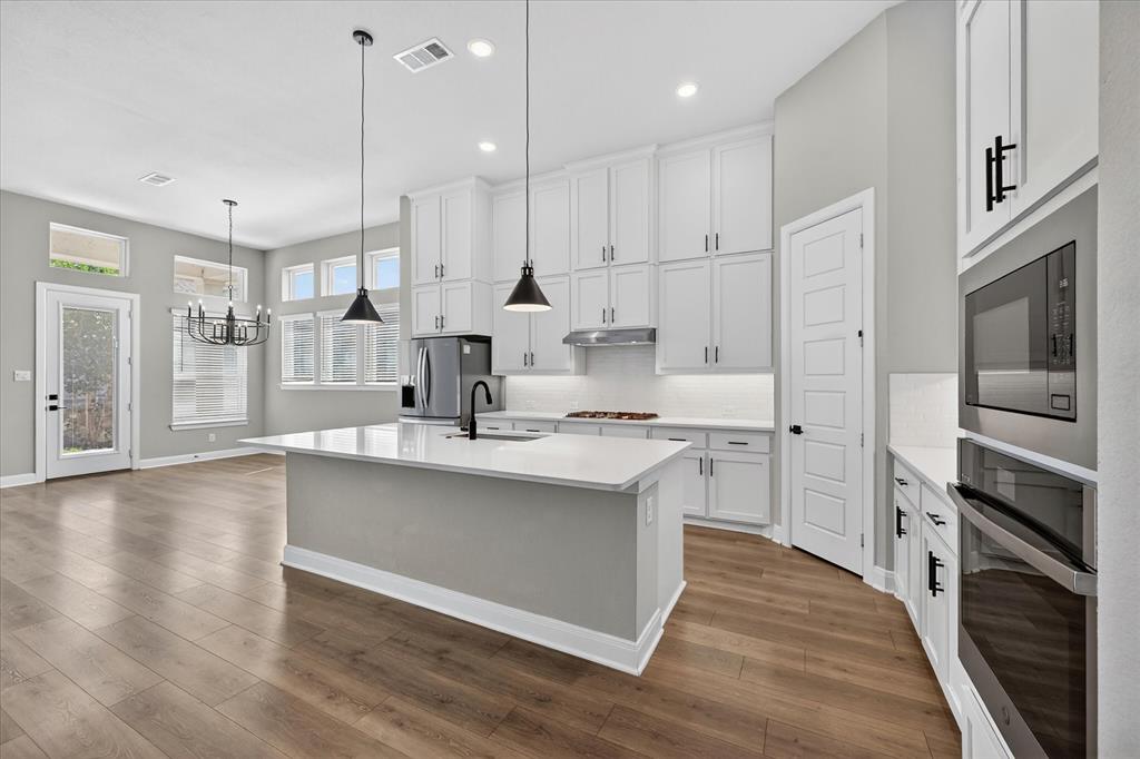 2237 Pika Road Northlake, TX 76247 - Photo 8 of 37 Open-concept kitchen featuring an oversized island with pendant lighting, white shaker cabinetry, stainless steel appliances, and wood-finish flooring