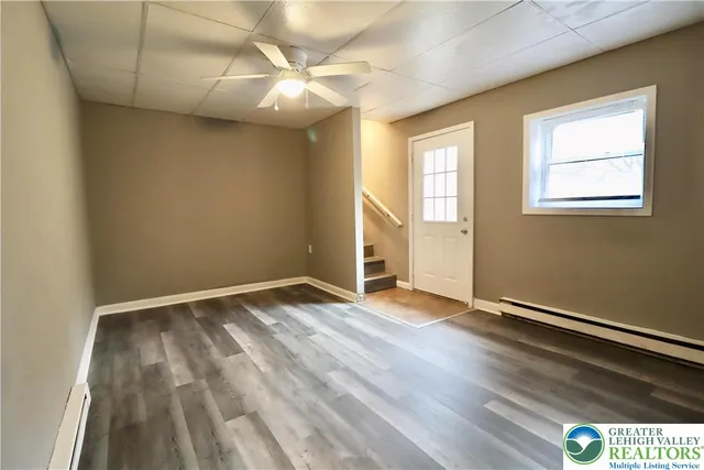 an empty room with wooden floor fan and windows