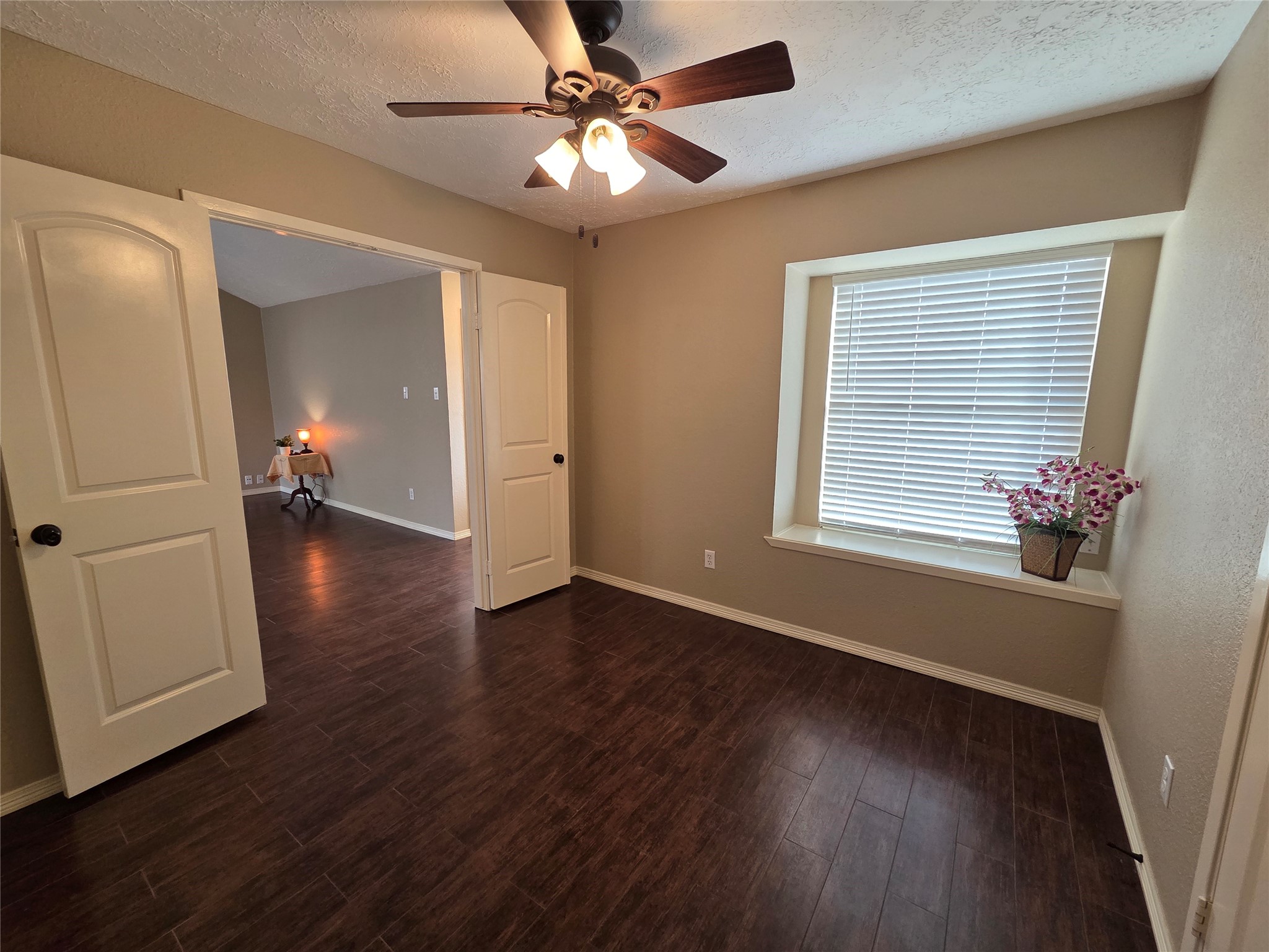 4203 Spinks Creek Lane Spring, TX 77388 - Photo 12 of 14 This bedroom/office features warm-toned walls and dark wood flooring, complemented by a ceiling fan with light. A large window with window seat and 2 inch blinds allows natural light, and double doors open to the living room, adding versatility to allow this room to be a bedroom or an office space.