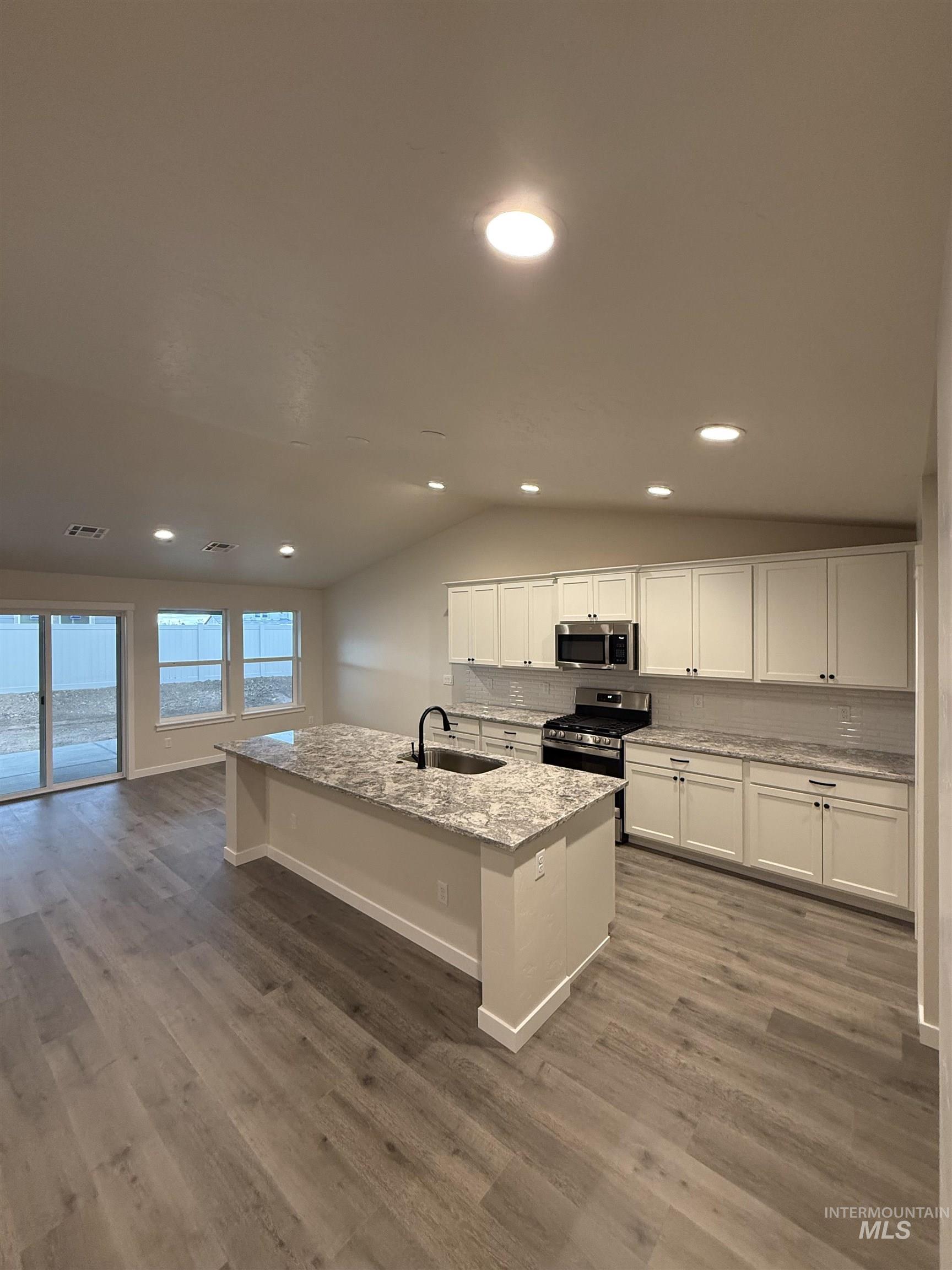 7819 East Meriwether Nampa, ID 83687 - Photo 2 of 12 Kitchen with decorative backsplash, vaulted ceiling, white cabinets, a center island with sink, and light stone countertops