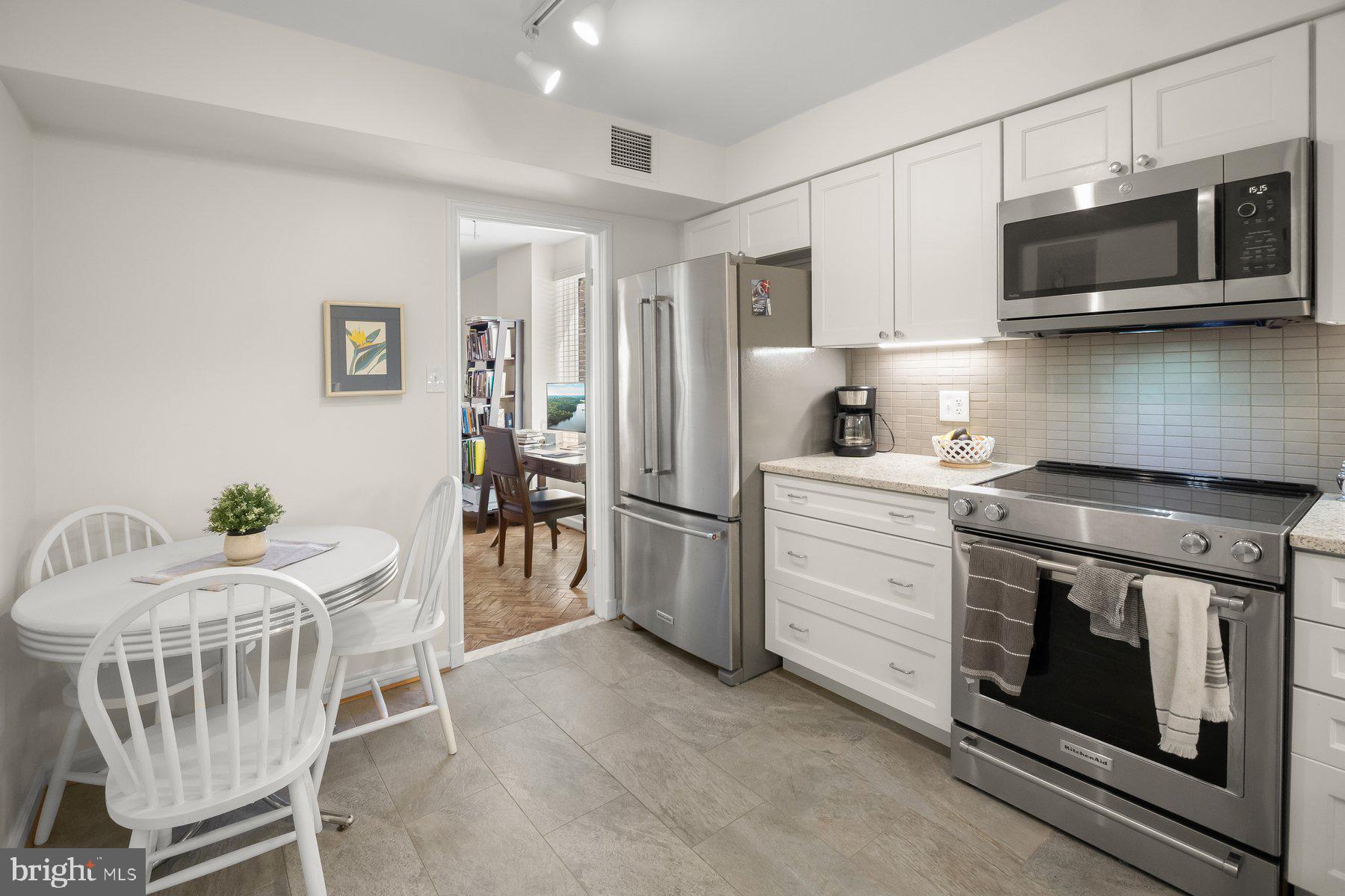 1045 31st Street Northwest, Unit 303 Washington, DC 20007 - Photo 7 of 12 a kitchen with stainless steel appliances kitchen island a white stove top oven a refrigerator with white cabinets and wooden floor