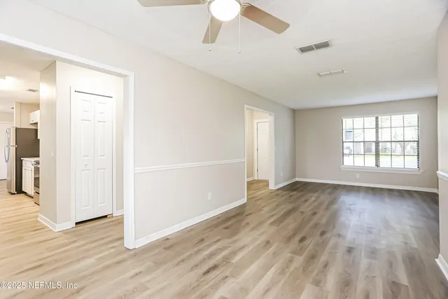 an empty room with wooden floor chandelier fan and windows