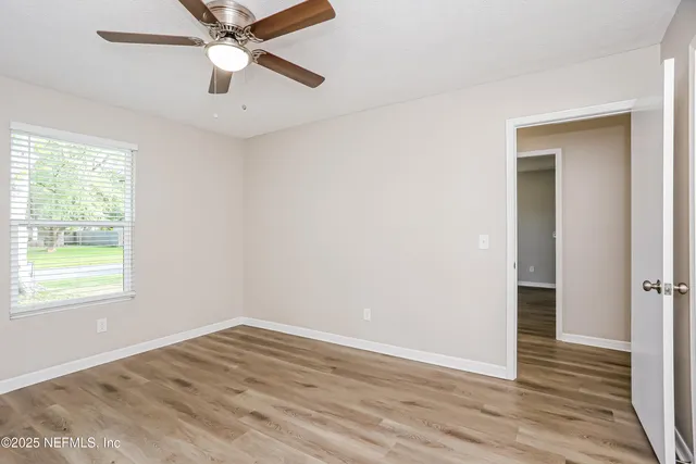 an empty room with wooden floor fan and windows