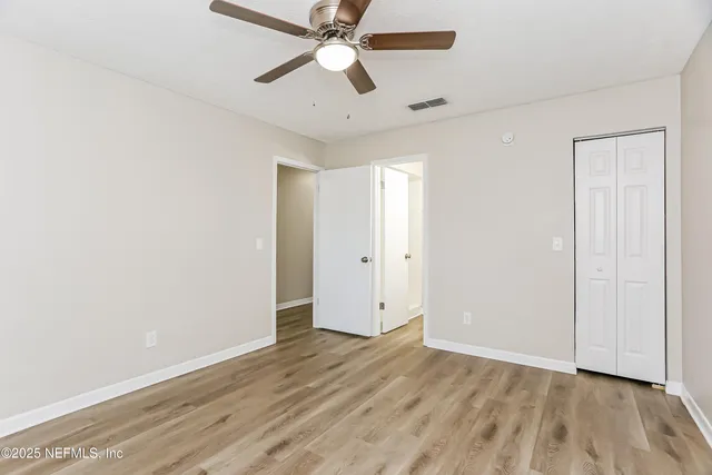 an empty room with wooden floor ceiling fan and windows