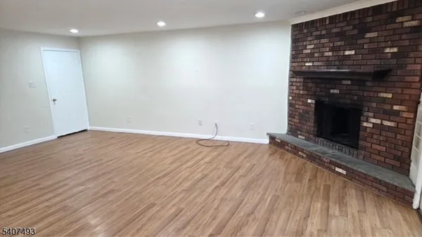 a view of an empty room with wooden floor and a fireplace