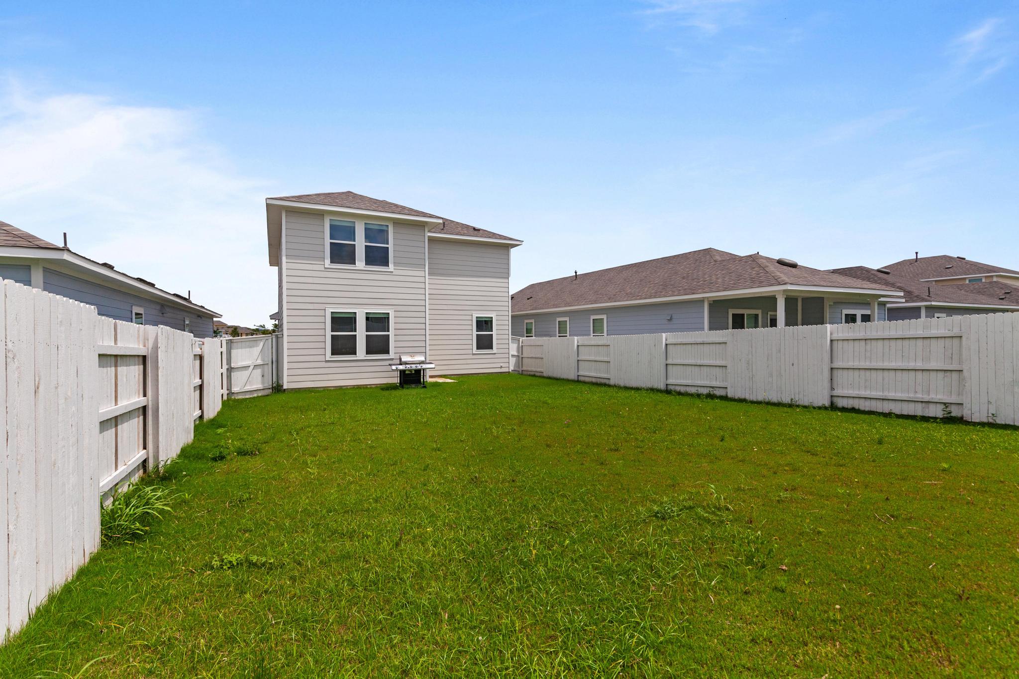 242 Barley Lane Elgin, TX 78621 - Photo 29 of 31 Spacious fenced backyard featuring a verdant lawn, a two-story home with light-colored siding, and a white privacy fence encompassing the property