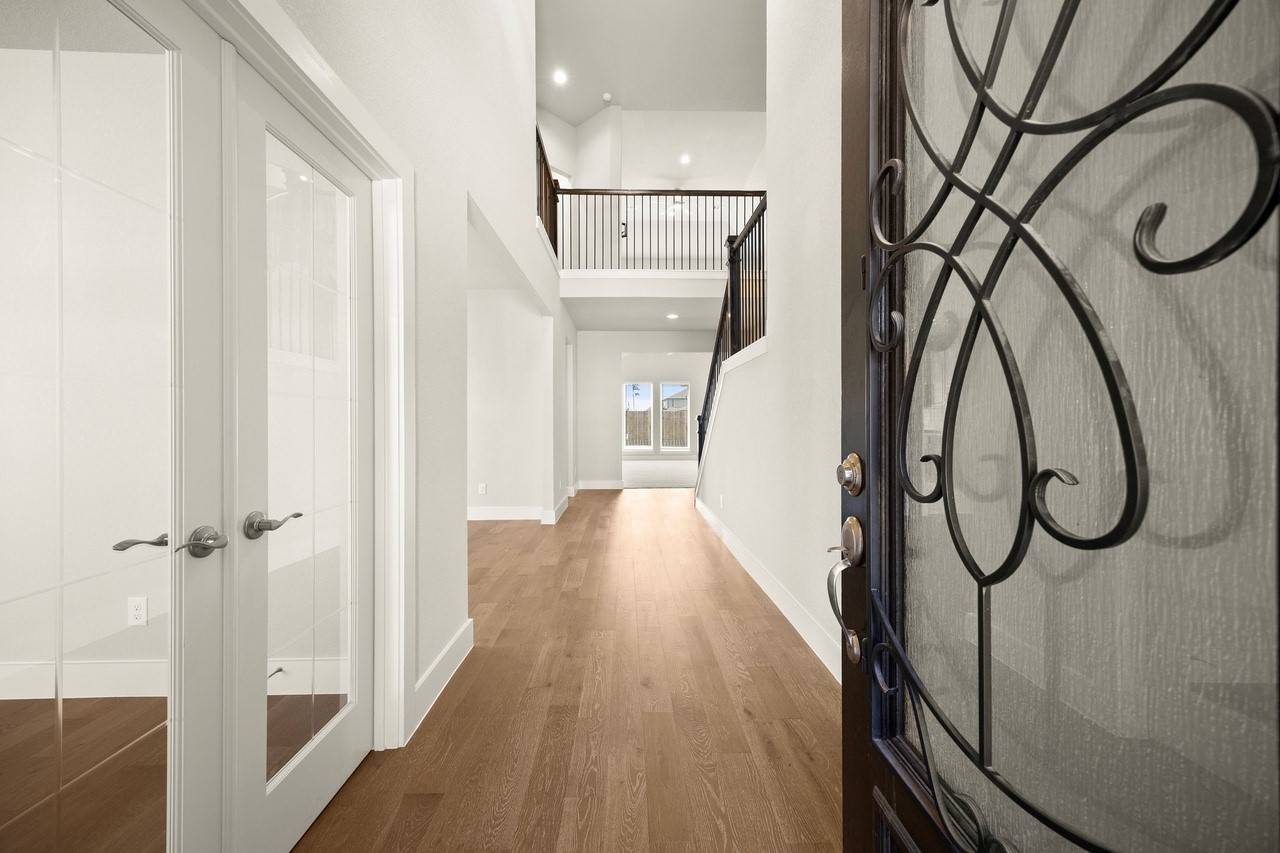 Enter a bright and spacious foyer featuring elegant wood flooring, high ceilings, and stylish wrought iron details, leading into a welcoming and open living area.