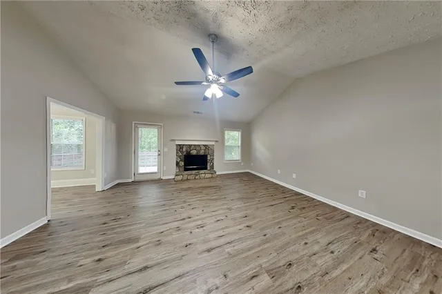 an empty room with wooden floor ceiling fan and windows