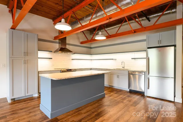 a kitchen with stainless steel appliances granite countertop a refrigerator a sink dishwasher a stove and white countertops with wooden floor