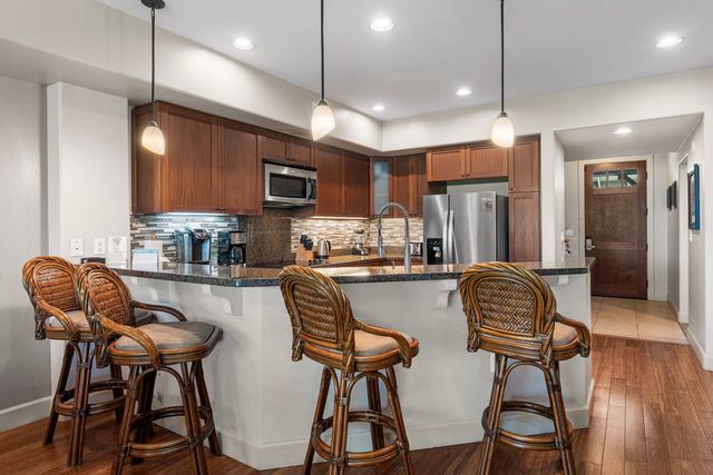 a kitchen with stainless steel appliances granite countertop a dining table chairs refrigerator and microwave