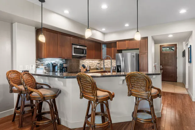 a kitchen with stainless steel appliances granite countertop a dining table chairs refrigerator and microwave