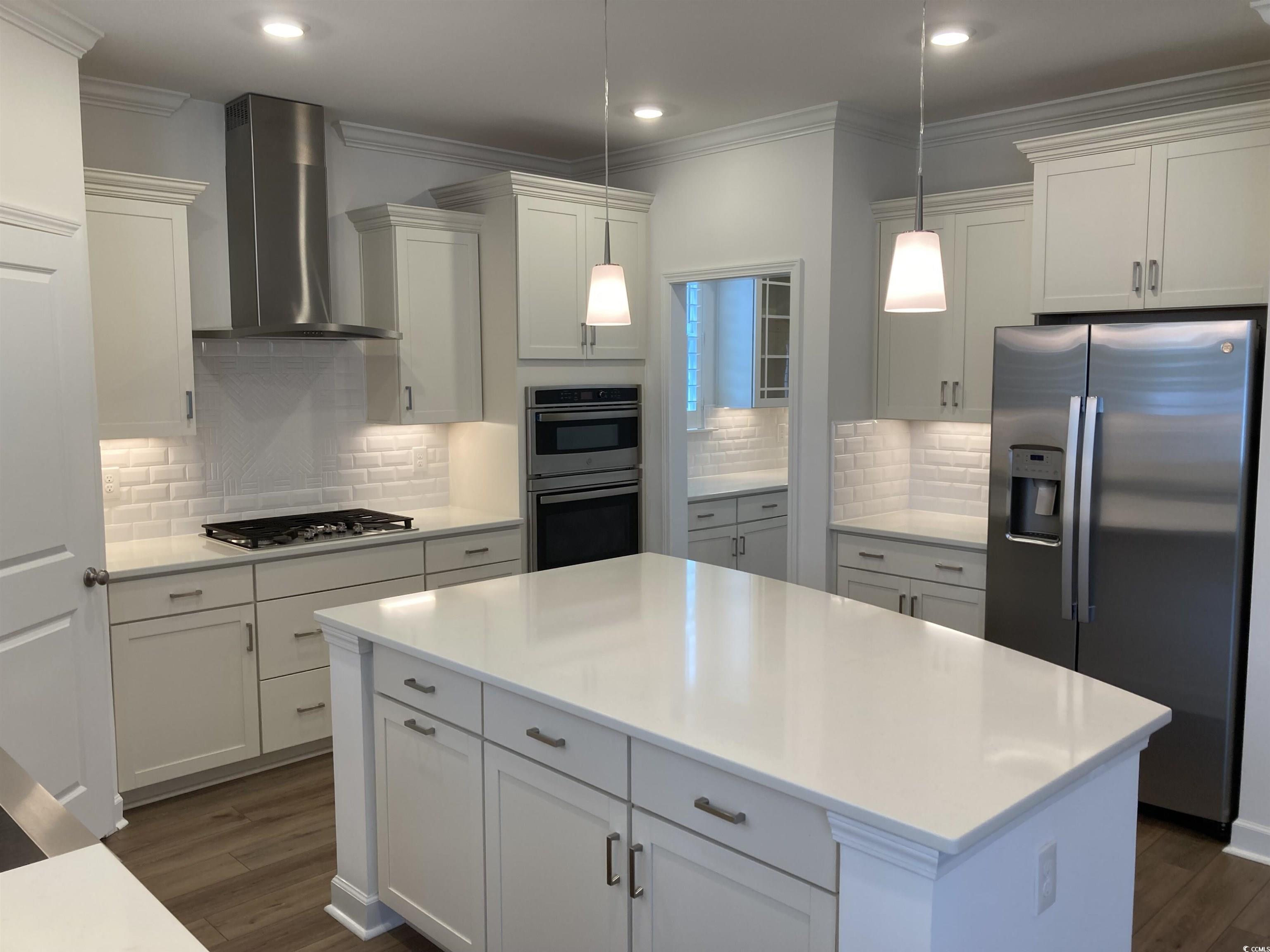 736 Enchantment Loop Myrtle Beach, SC 29588 - Photo 15 of 39 Kitchen with appliances with stainless steel finishes, wall chimney exhaust hood, white cabinetry, ornamental molding, and a kitchen island