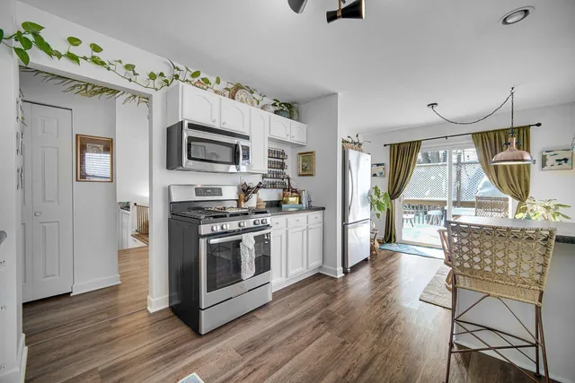 a kitchen with stainless steel appliances granite countertop a stove top oven a sink a dining table and chairs with wooden floor