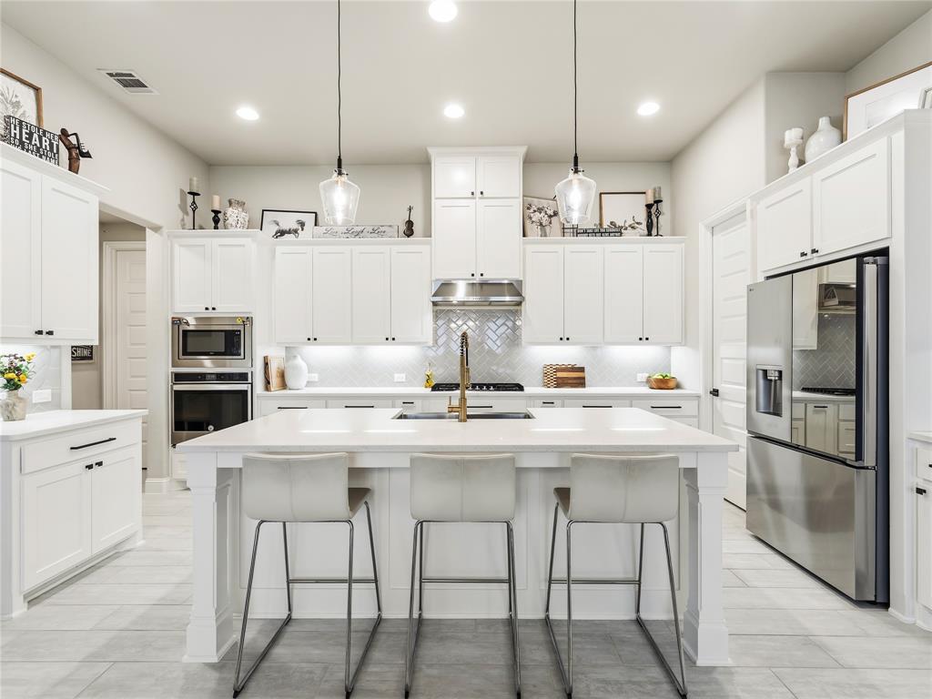 15340 Crape Myrtle Road Frisco, TX 75035 - Photo 9 of 40 Spacious kitchen featuring an expansive center island, white shaker cabinetry, stainless steel appliances, herringbone tile backsplash, and recessed lighting
