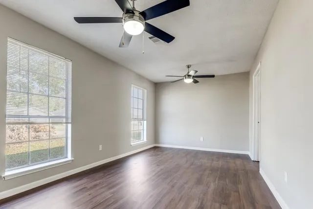 an empty room with wooden floor fan and windows