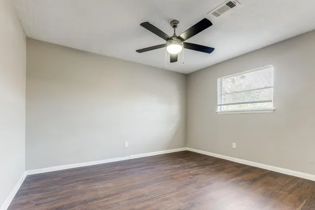 an empty room with wooden floor fan and windows