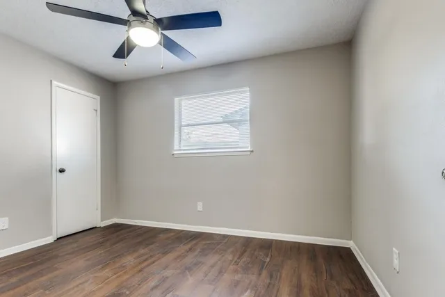 an empty room with wooden floor ceiling fan and windows