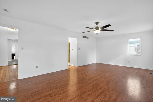 a view of an empty room with wooden floor and a ceiling fan