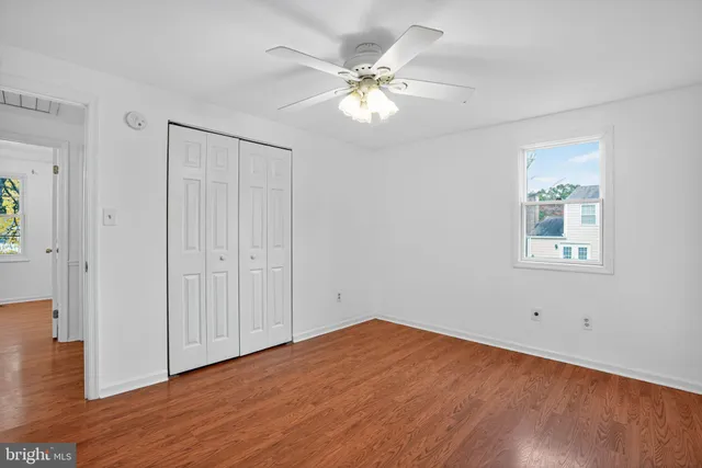 an empty room with wooden floor chandelier fan and windows