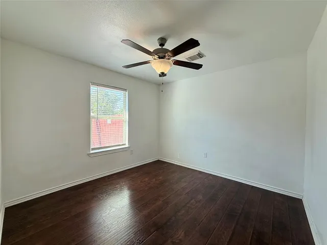 an empty room with wooden floor fan and windows