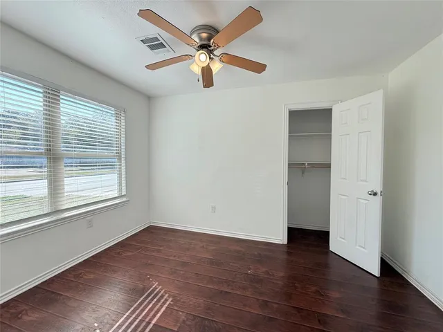 an empty room with wooden floor chandelier fan and windows