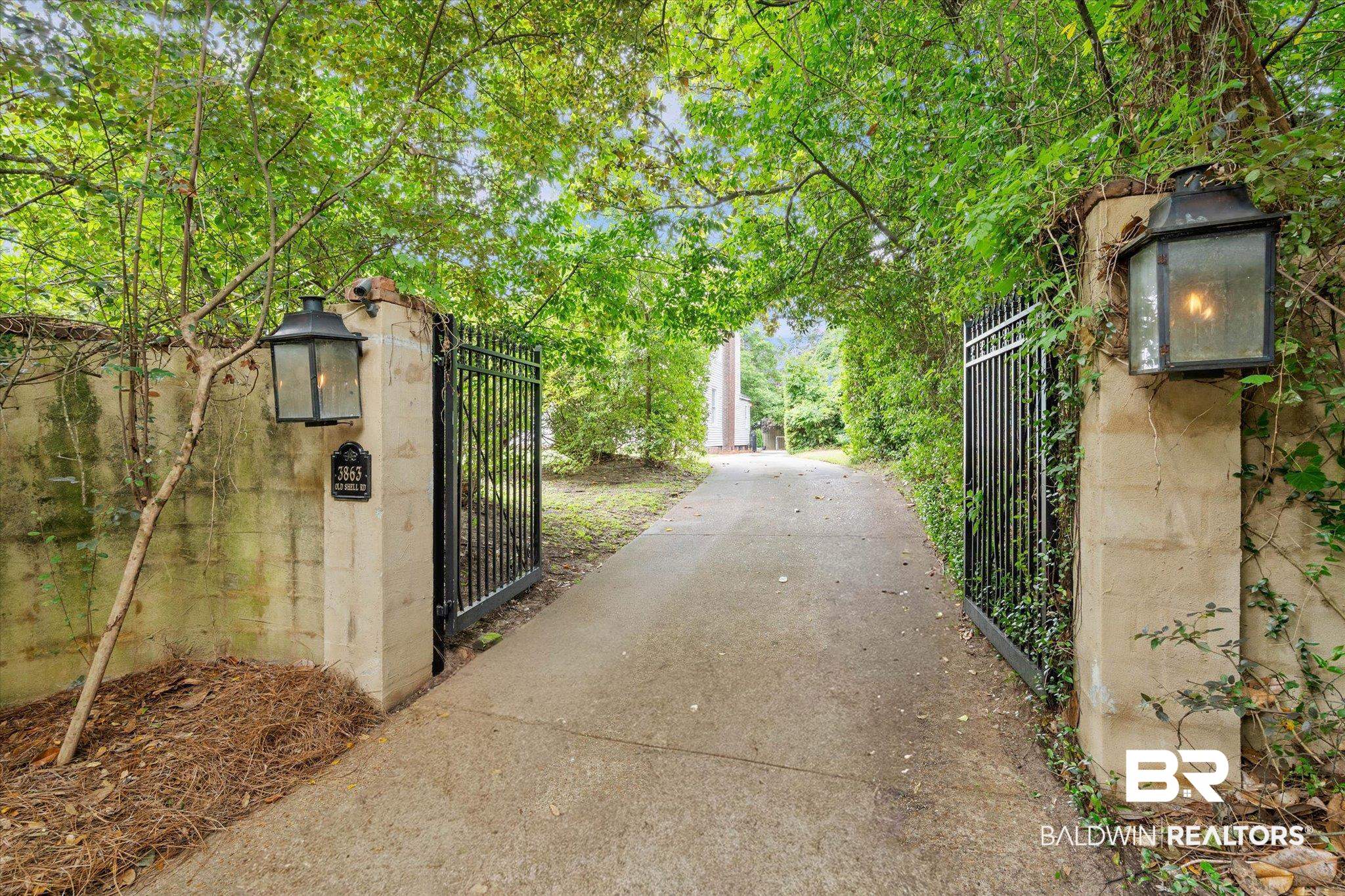 3863 Old Shell Road Mobile, AL 36608 - Photo 38 of 48 Private driveway entrance featuring stone pillars with integrated lanterns and wrought iron gates, bordered by mature trees and lush greenery