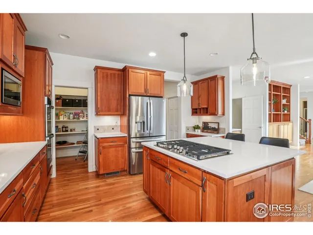 a kitchen with stainless steel appliances granite countertop a stove a sink dishwasher a refrigerator and wooden cabinets with wooden floor