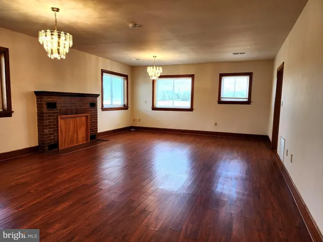 an empty room with wooden floor chandelier and windows