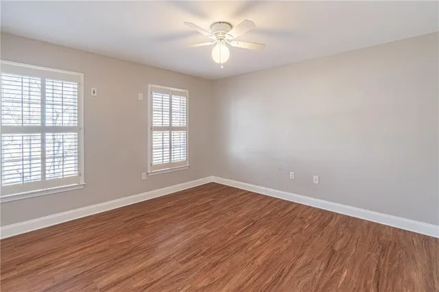 an empty room with wooden floor fan and windows
