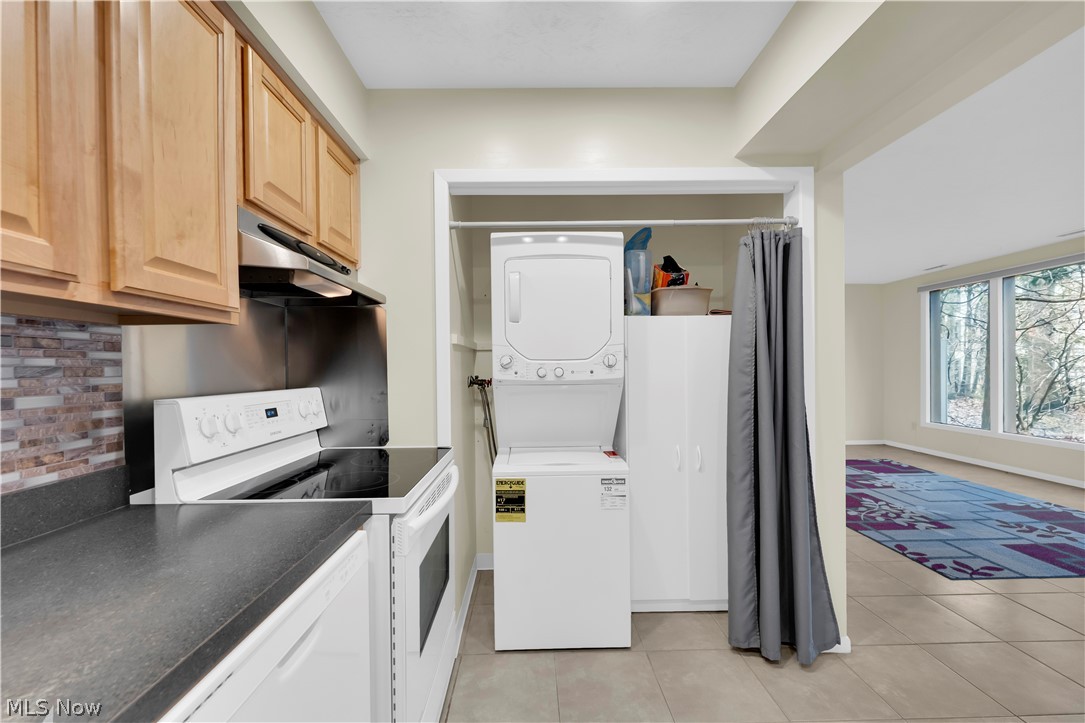 985 Canyon View Road, Unit 108D Northfield, OH 44067 - Photo 9 of 18 Kitchen featuring white appliances, stacked washing machine and dryer, light wood finish cabinets, dark countertops, and light tile patterned floors