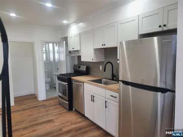 a kitchen with stainless steel appliances granite countertop a refrigerator a sink and white cabinets
