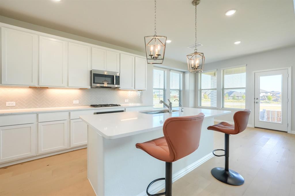 1309 Buttercup Road Prosper, TX 75078 - Photo 15 of 36 a kitchen with stainless steel appliances granite countertop a stove a sink dishwasher a dining table and chairs with wooden floor