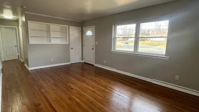 an empty room with wooden floor closet and windows