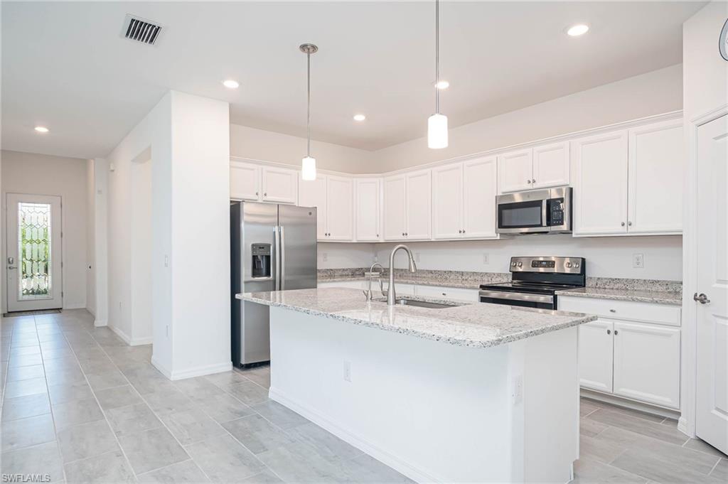2418 Orchard Street Naples, FL 34120 - Photo 7 of 35 Kitchen featuring light stone counters, stainless steel appliances, a kitchen island with sink, sink, and white cabinets