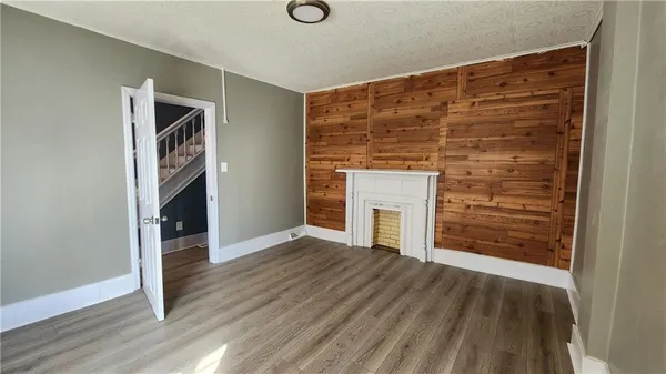 a view of an empty room with wooden floor fireplace and a window