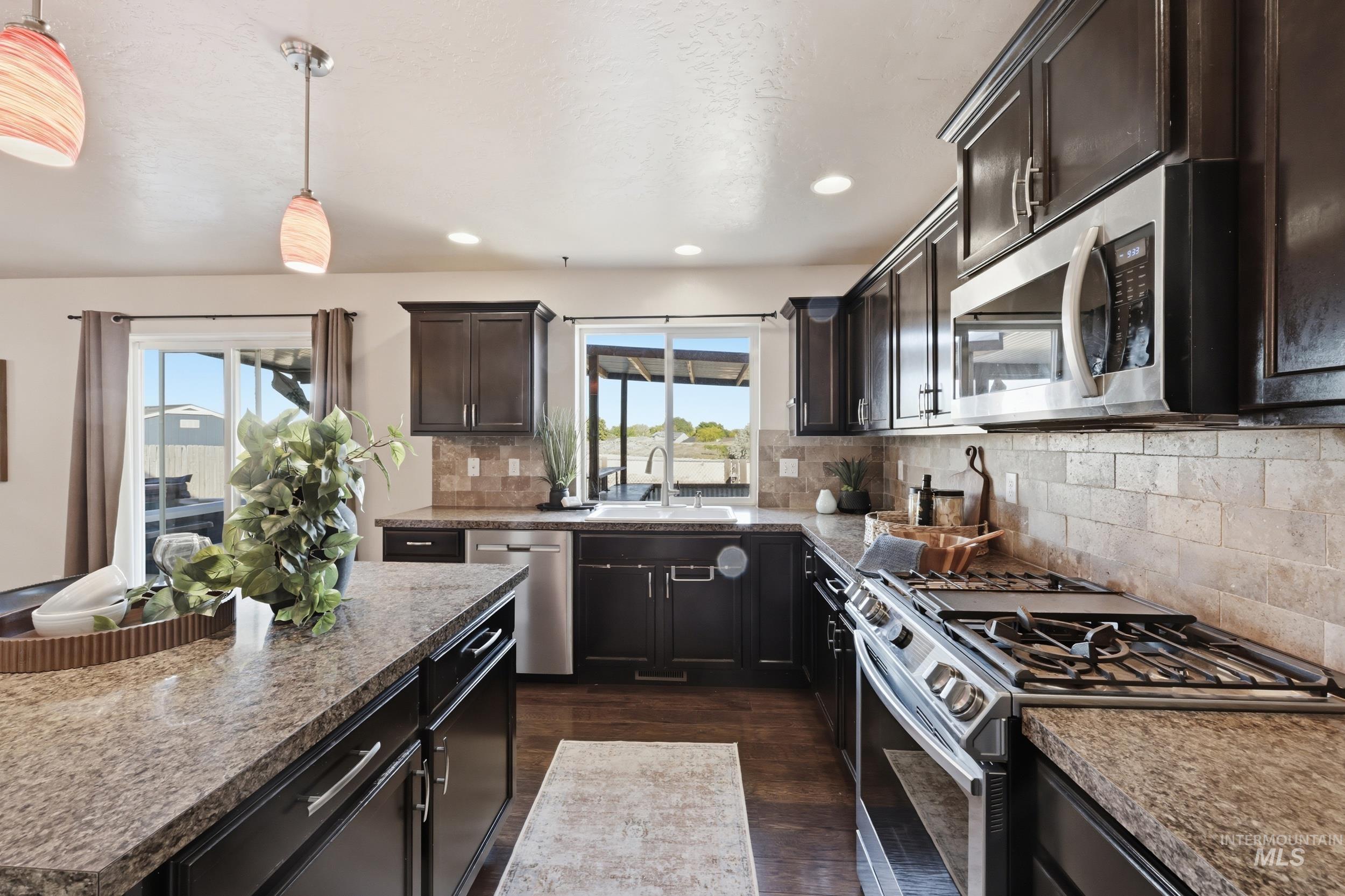 4855 South Chex Way Boise, ID 83709 - Photo 12 of 47 Modern kitchen featuring dark wood cabinetry, stainless steel appliances, and a tiled backsplash