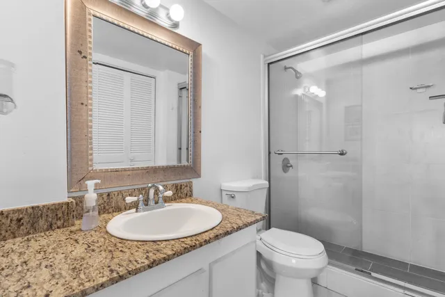 a bathroom with a granite countertop sink toilet a mirror and shower